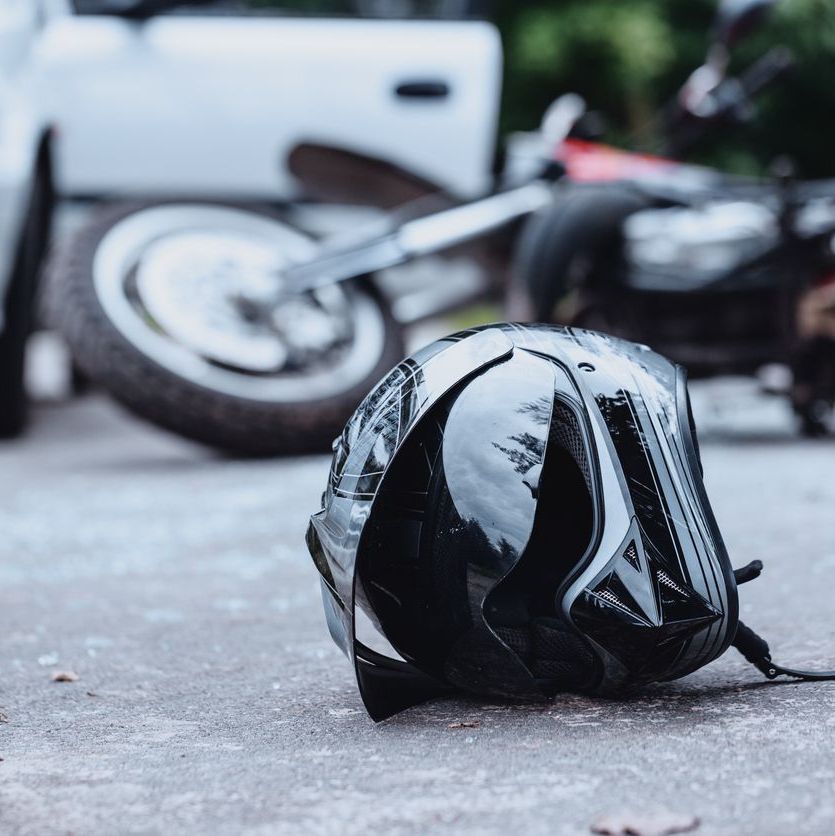 Close-up of a black biker helmet on the street with overturned motorbike in the background