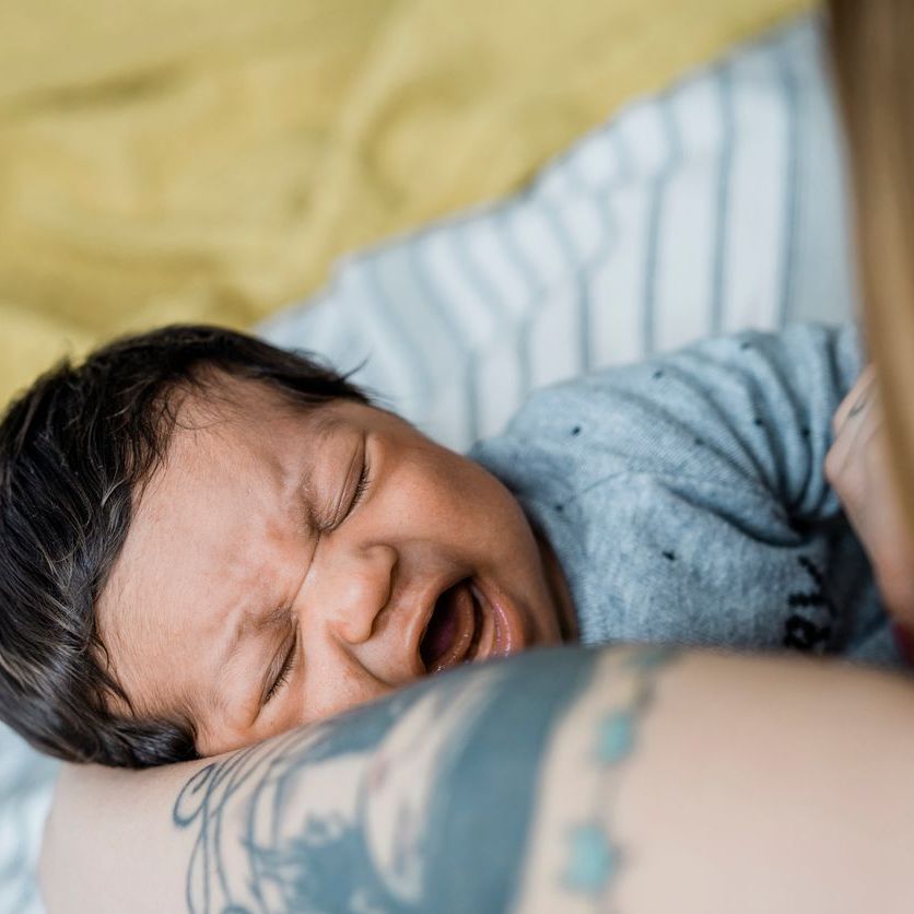 Close-up of a crying little baby in the arms of her mother.